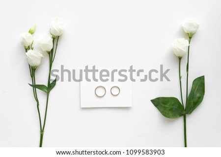 Wedding card with wedding rings and roses, on white marble . Top view.