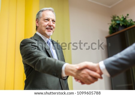 Senior manager welcoming a colleague in his office by shaking his hand in sign of friendship
