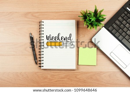 Weekend loading text on white sheet and office supplies on wooden table. Top   view Royalty-Free Stock Photo #1099648646