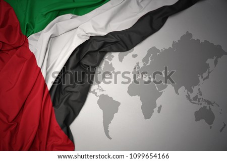 waving colorful national flag of united arab emirates on a gray world map background.