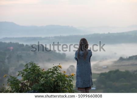 A woman in cloth suit stand and see view and take a picture in the morning while the could flow between mountain 