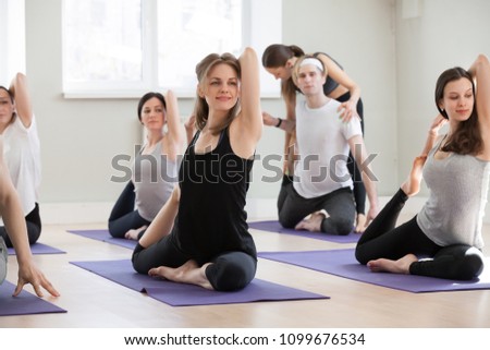 Young sporty female yoga instructor teaching Eka Pada Rajakapotasana exercise for a group of yogi people practicing in studio, working out indoor, teacher helping to master One Legged King Pigeon pose