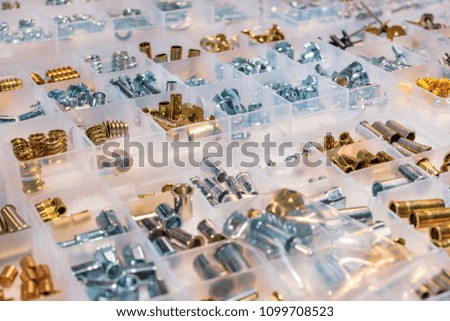 Many screws arranged as background. Metal fasteners, scattered in plastic cells.
