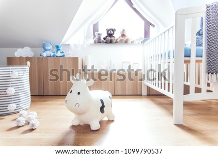 Modern scandinavian nursery interior with toys, teddy bears, baby cot and cotton lamps. Sunny and bright room.