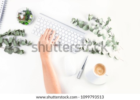 Flat lay home office workspace, someone hand typing on white keyboard and silver green twigs