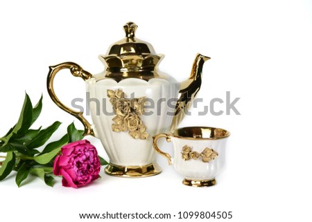 A white teapot with a golden flower, a milk jug, a cup of tea and a beautiful lilac peony.