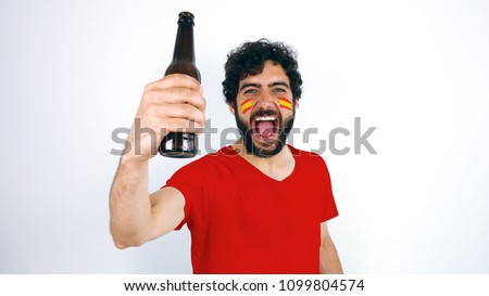 Sport fan holding a beer screaming for the triumph of his team. Man with the flag of Spain makeup on his face and red t-shirt.                    