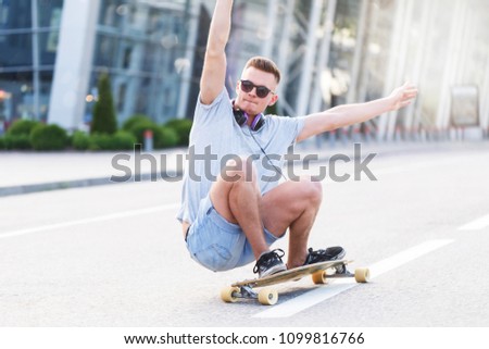 Skateboarder in sunglasses rides longboard on asphalt road before modern building in the city, low position trick ride
