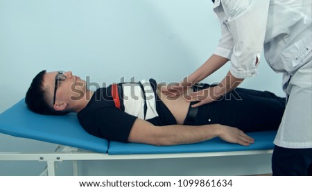Female doctor examining the abdomen of male patient lying on the hospital sofa