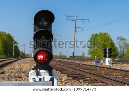 Traffic lights on ground level at the raiway. Red light is turned on. Railroad on a sunny day at  the background.