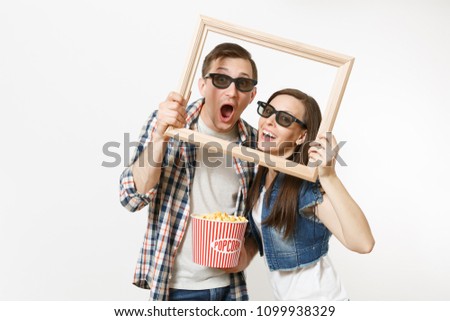 Young happy couple, woman and man in 3d glasses and casual clothes watching movie film on date, holding bucket of popcorn and picture frame isolated on white background. Emotions in cinema concept