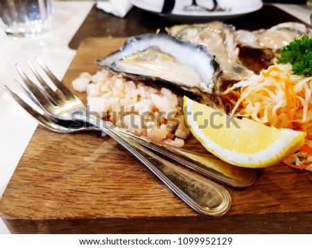 Close up fresh oyster with two forks, vegetables and sliced of yellow lemon on the wooden plate. Seafood and Lunch Time concept