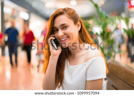 Young redhead pretty girl in a shopping center keeping a conversation with the mobile phone with someone