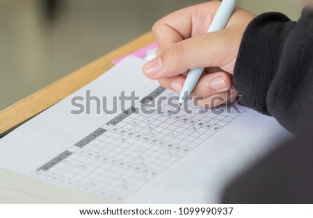 Education test concept : Hands with pen over application form, Students taking exams, writing examination room with undergraduate inside. Student sitting learning lessons doing final in classroom