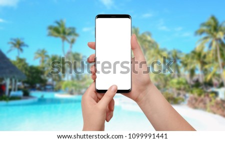 Female hands holding smartphone with empty screen, tropical pool in background