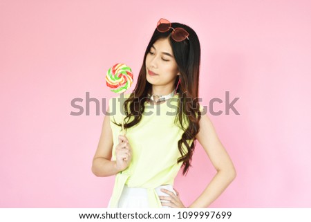 beautiful portrait Asian girl in casual clothes with beaming smile holding colorful lollipop on pink background