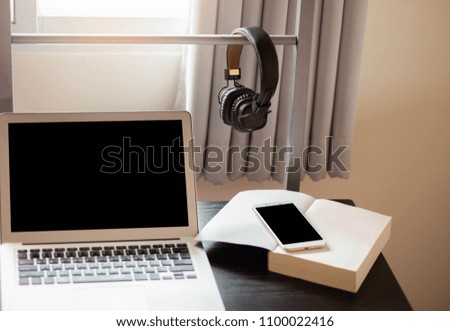 Close up leather headphone on wooden desk,blank screen laptop with white mobile phone on book,education or business concept,selective focus.