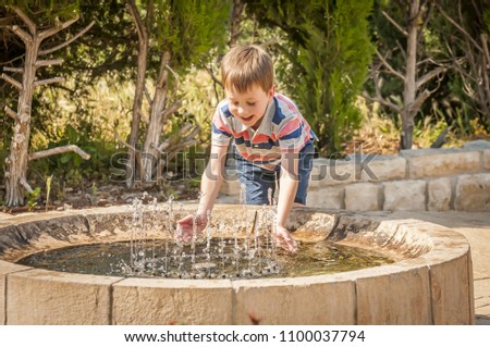 Happy cute Caucasian kid playing with water fountain in the public park. Water game.