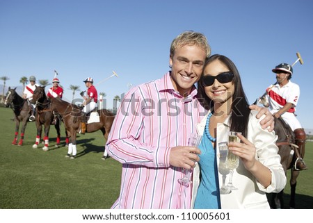 Portrait of couple holding champagne glass with polo players in the background