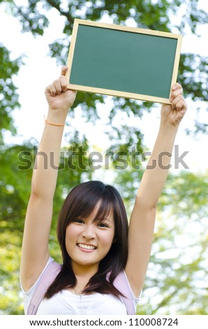Young Asian college girl arms up holding a blackboard outdoor, green park