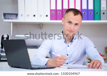 I am listening really carefully. Portrait of a young male manager at the office with a laptop. He sits right in front of the camera and looks serious.