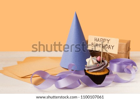Delicious cupcake, gift and cap on yellow background, copy space. Birthday, party, holiday concept