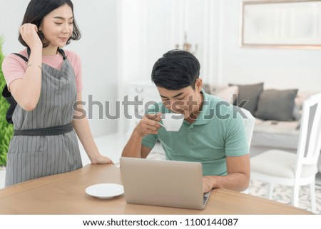 Asian couple at home using a laptop with coffee cup. The men sitting at a table.