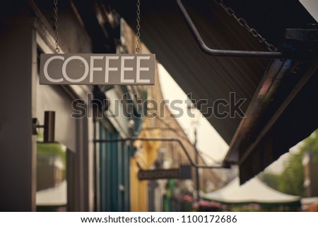 A Scandinavian design wooden coffee sign hanging outside a shop with the blurred background. Landscape format.