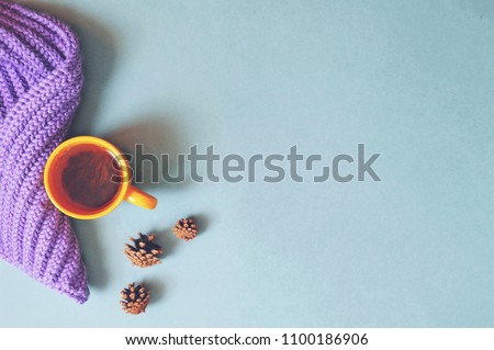 Cozy autumn or winter background. Cup of green tea, purple woolen scarf and pine cones on a blue background. Free space for text, mockup