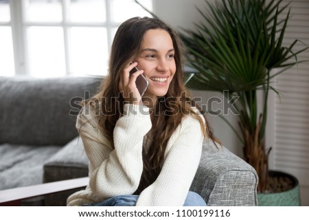 Smiling millennial woman talking on the phone at home, happy young girl holds cellphone making answering call, attractive teenager having pleasant conversation chatting by mobile with friend Royalty-Free Stock Photo #1100199116