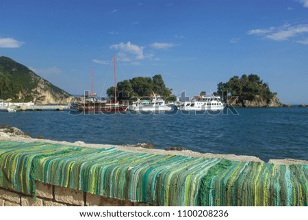 Parga town looking at the boats at the background moored at the dock while sitting at a cafe in front of a colorful rug at a bench made of stones