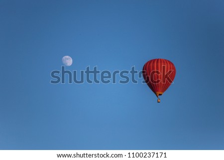 full moon big red balloon with a basket and with people flying in a clear blue sky without clouds next to the full moon