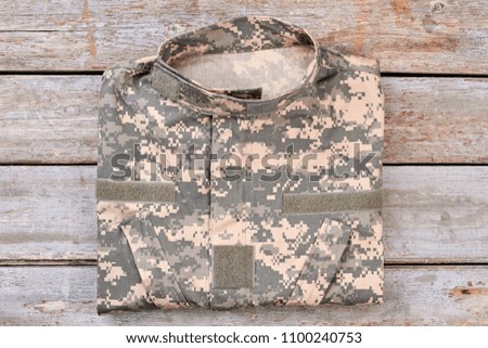 Folded camouflage military jacket. Top view, flat lay. Wooden desk background.