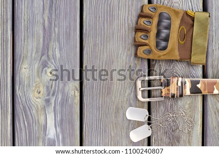 Fingerless glove, belt and steel dog tags. Grey wooden background with copyspace. Top view, flat lay.