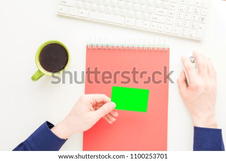 white Desktop, male hands, guy holding a business card, man working at the computer, notebook, white background with copy space, for advertisement, top view
