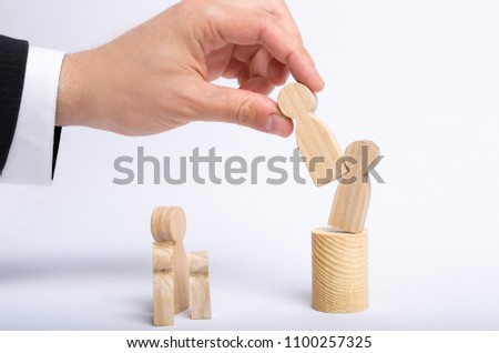 The man's hand of a businessman in a business suit holds a wooden figure of a man in his hand and moves another figure from his post. concept of firing an employee, the replacement of staff.