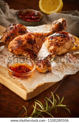 Crispy grilled seasoned chicken legs or drumsticks fresh from the summer barbecue with a spicy marinade and rosemary on crumpled paper on a wooden board
