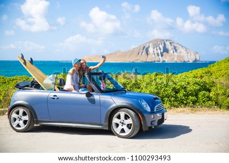 
Car road trip vacation young people taking selfie photo with phone during summer travel vacation. Tourists couple taking photos on Hawaii in convertible car, with smartphone camera