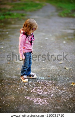 Little girl looking at a chalk drawing in a park