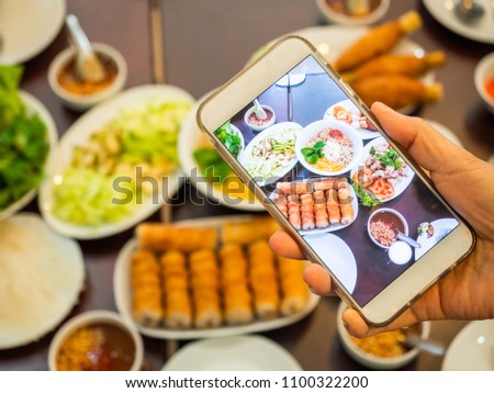 hand holding mobile phone take photo food.Namnaung traditional Vietnamese food with appetizer,salad on table top view. 