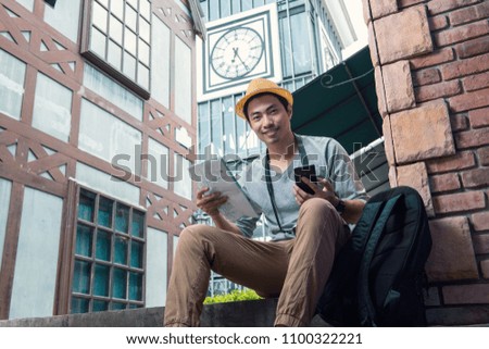 Asian young handsome traveller sits and reads city map with gps on mobile phone in vintage city