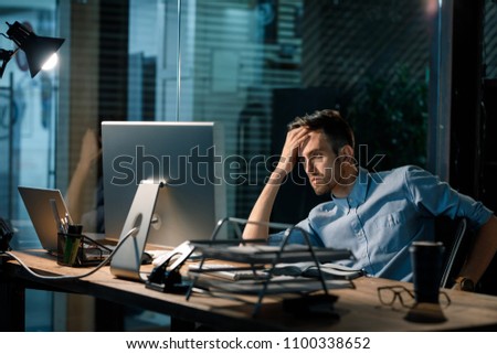 Man sitting alone in office late at night watching computer and solving problem working overhours.  Royalty-Free Stock Photo #1100338652