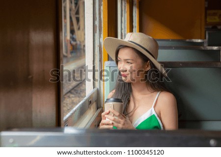 A beautiful charming asian girl in casual panama hat holding a cup of coffee. Gorgeous woman sit beside widow in retro train in morning. Feeling look happy and relax. Portrait lady on travel concept.