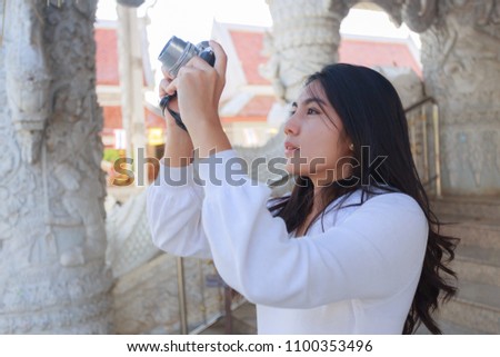 Asian woman in a white dress taking photo with mirrorless camera at Buddhist Temple