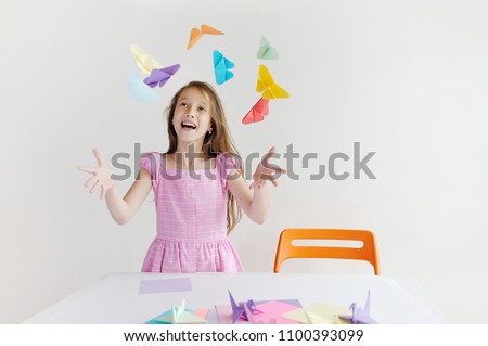 The happy girl plays with paper of origami. The girl plays the fool Royalty-Free Stock Photo #1100393099