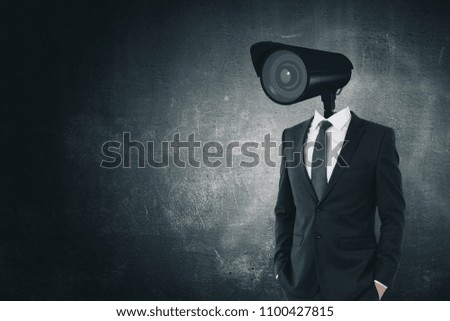 CCTV camera headed businessman standing on dark concrete background with copy space. Supervision and spy concept Royalty-Free Stock Photo #1100427815