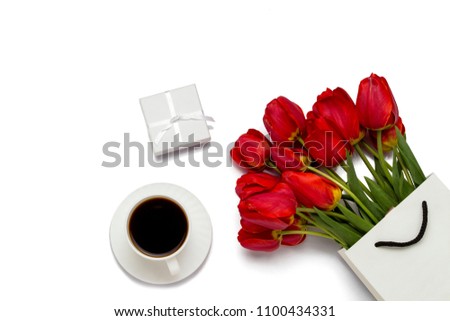 Red tulips in a paper gift bag, gift box and a cup of coffee on a white background. Top View