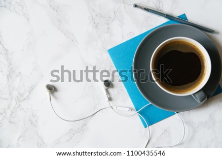 Workplace flatlay with coffee cup, papers and earphones on marble table
