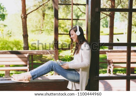 Young successful businesswoman in light casual clothes. Woman working on modern laptop pc computer, listen music in headphones on head in street outdoors. Mobile Office. Freelance business concept
