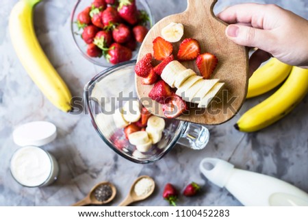 Ingredients for making strawberry banana smoothies on a gray table next to a glass bowl of blendet. Cooking a healthy breakfast concept. TOp view, flat lay Royalty-Free Stock Photo #1100452283